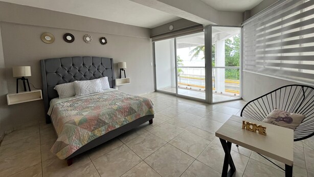 A modern bedroom with a large bed, bedside tables, a chair, and a view of the outdoors. - Estudio con vista al mar en Cozumel A1 (San Miguel de Cozumel)