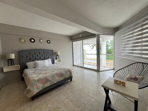 Une chambre à coucher moderne avec un grand lit, des tables de chevet, un fauteuil et une vue sur l’extérieur.