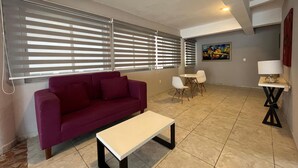 A living room with a purple sofa, a white coffee table, a dining table with two chairs, and a painting on the wall. - Estudio con vista al mar en Cozumel A1 (San Miguel de Cozumel)