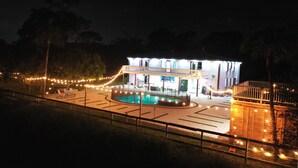 Un edificio de dos pisos con piscina en el centro, rodeado por una terraza y luces colgantes.