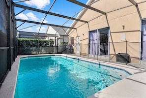 Uma piscina com cobertura de vidro, um espaço de varanda coberto e um edifício com fachada bege.