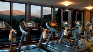 Un gimnasio con cintas de correr y elípticas, amplias ventanas con vistas a la montaña y luces en el techo.