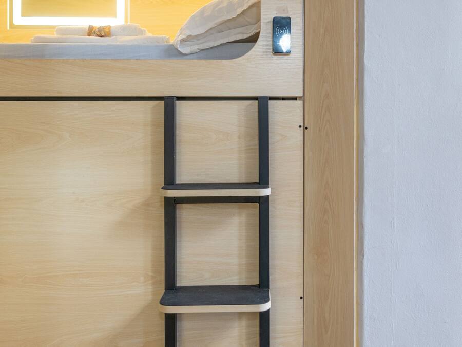 Una cama litera con cabecera de madera, una mesita de noche y una estantería empotrada.