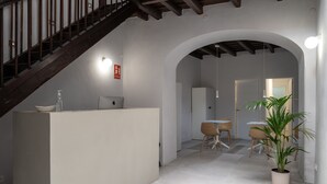 A modern interior with a staircase, a reception desk, a dining area, and a potted plant.