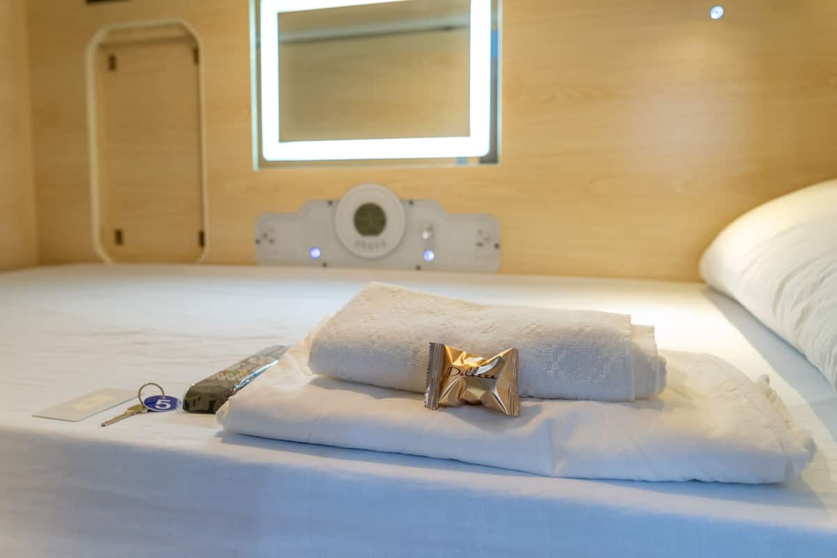 Cama bem arrumada com uma toalha branca enrolada e um pequeno objeto dourado em cima.