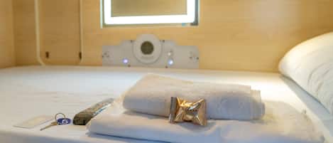 Una cama bien hecha con una toalla blanca enrollada y un objeto pequeño dorado encima.