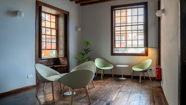 A room with wooden flooring, two windows with wooden frames, and three chairs.