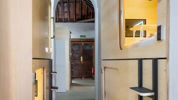 A narrow hallway with wooden walls, a dark floor, and a door at the end. Shelves are mounted on the walls, and a small shelf is attached to the right wall.