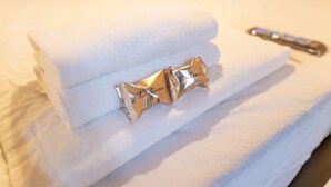 A neatly folded white towel with a decorative gold tag labeled "Delizia" on a bed.
