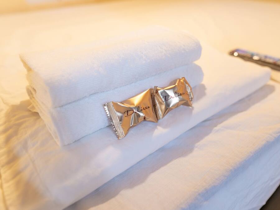 A neatly folded white towel with a decorative gold tag labeled "Delizia" on a bed.