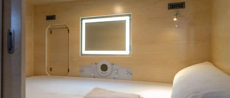 Una habitación de hotel con una cama, una mesita de noche, un espejo y un reloj de pared.