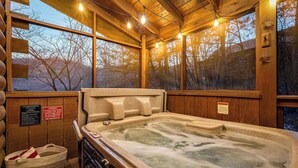 A wooden cabin with a hot tub, large windows, and a view of trees. - Timeless Tranquility-Screened Hot Tub-5 Min to Parkway-Pet Paradise-Dog Run! (Pigeon Forge)