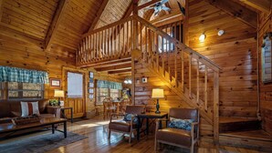 A log cabin interior with a wooden staircase, a dining area, and a living room with a sofa and chairs. - Timeless Tranquility-Screened Hot Tub-5 Min to Parkway-Pet Paradise-Dog Run! (Pigeon Forge)