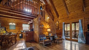 A spacious wooden cabin with a dining area, a living room with a fireplace, and a staircase leading to an upper level. - Timeless Tranquility-Screened Hot Tub-5 Min to Parkway-Pet Paradise-Dog Run! (Pigeon Forge)