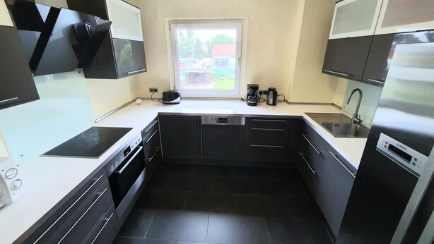A modern kitchen with black cabinets, a window, a Bosch coffee maker, and a dishwasher. - Apartment Pottmensch near Centro with parking lot (Oberhausen)