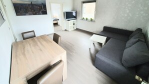 A modern living room with a wooden dining table, a gray sofa, and a TV on a white stand. - Apartment Pottmensch near Centro with parking lot (Oberhausen)