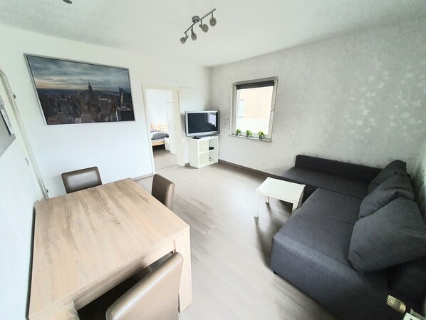 A modern living room with a wooden dining table, a gray sofa, and a TV on a white stand. - Apartment Pottmensch near Centro with parking lot (Oberhausen)