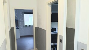 A narrow hallway leading to a kitchen area with a microwave and a trash bin. - Apartment Pottmensch near Centro with parking lot (Oberhausen)