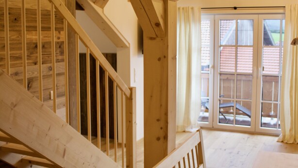 Een houten trap die leidt naar een balkon met uitzicht op een gebouw met rode daken.