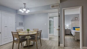 A dining area with a round table, chairs, and a chandelier. There is a door leading to a bedroom with a bed and a nightstand. - Newly renovated, free WIFI/PARKING, 10 min to the beach! (Clearwater)