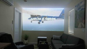 Un salón con una pantalla grande que muestra un avión y el texto 'JUST OK IS NOT OK'.