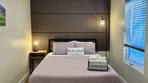 Un dormitorio ordenado con cama, mesitas de noche y una ventana con persianas.