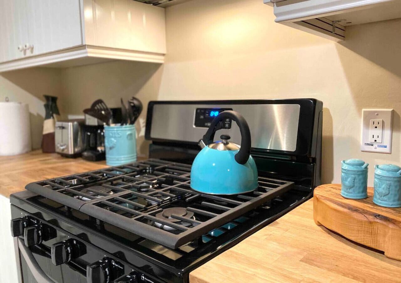 Een keuken met een gasfornuis, waterkoker en een houten snijplank.