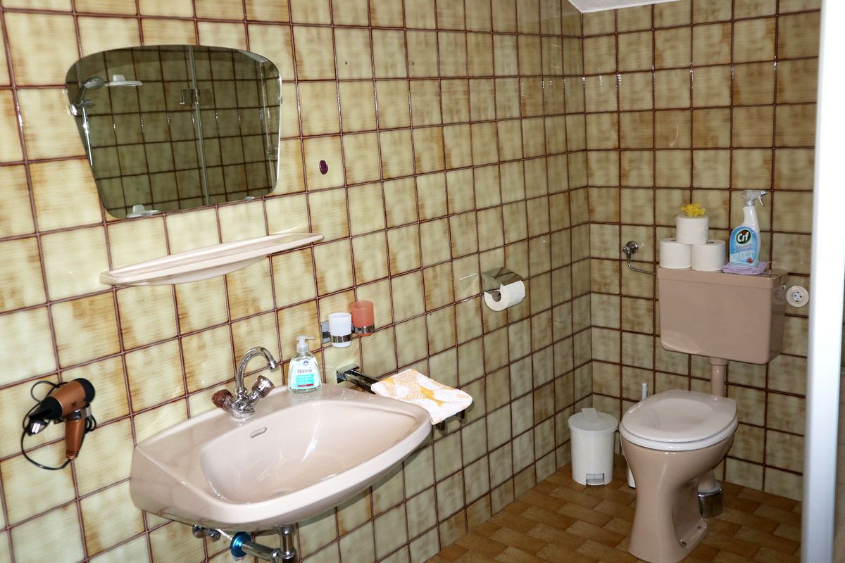 A bathroom with a sink, mirror, toilet, and tiled walls.