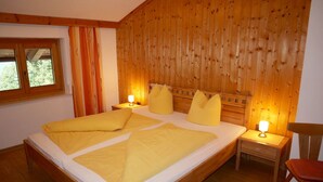 Una stanza con un letto di legno, due comodini con lampade, una finestra con tende e una sedia.