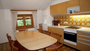 Una cucina compatta con tavolo, sedie, frigorifero, fornello e una finestra con tende.