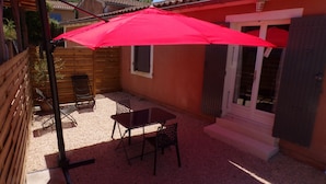 A patio with a red umbrella, a table, and two chairs.