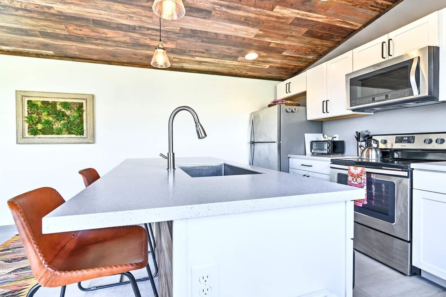 A modern kitchen with a central island, stainless steel appliances, and a rustic ceiling.