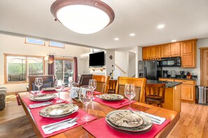Un coin repas avec une table en bois dressée pour quatre personnes, entourée de chaises, et un espace cuisine doté de meubles en bois et d’appareils électroménagers modernes.