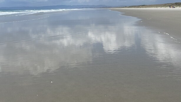 Una playa con una amplia orilla arenosa y olas suaves.