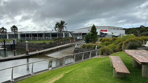 Un paseo ribereño con un puente de piedra, una zona ajardinada y un edificio con un cartel que dice "MARSHES ONE MARINE STORE".