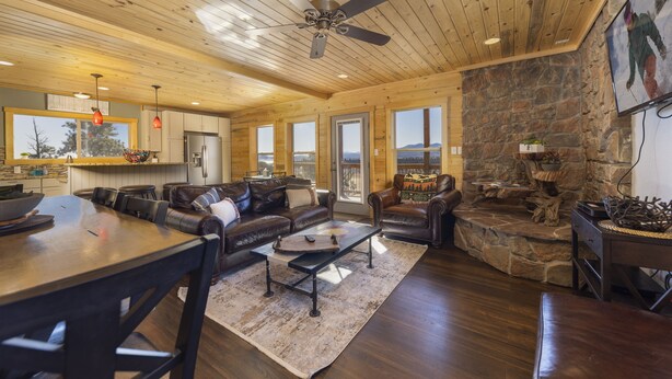 A spacious living area with a stone fireplace, leather sofas, and a wooden ceiling.