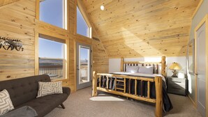 A wooden cabin bedroom with a bed, a sofa, and a window with a view.