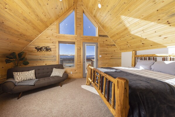 Een gezellige kamer met een schuine kap, houten wanden, een bed, een sofa en grote ramen met uitzicht.