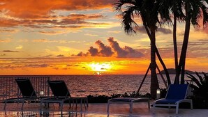 Blick auf einen Sonnenuntergang von einem Poolbereich mit Liegestühlen und Palmen.