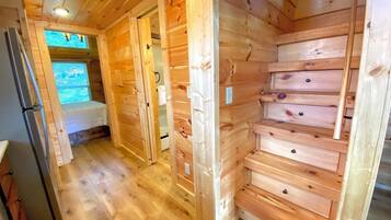 A wooden cabin interior with a hallway leading to a bedroom, a built-in wooden cabinet, and a refrigerator.