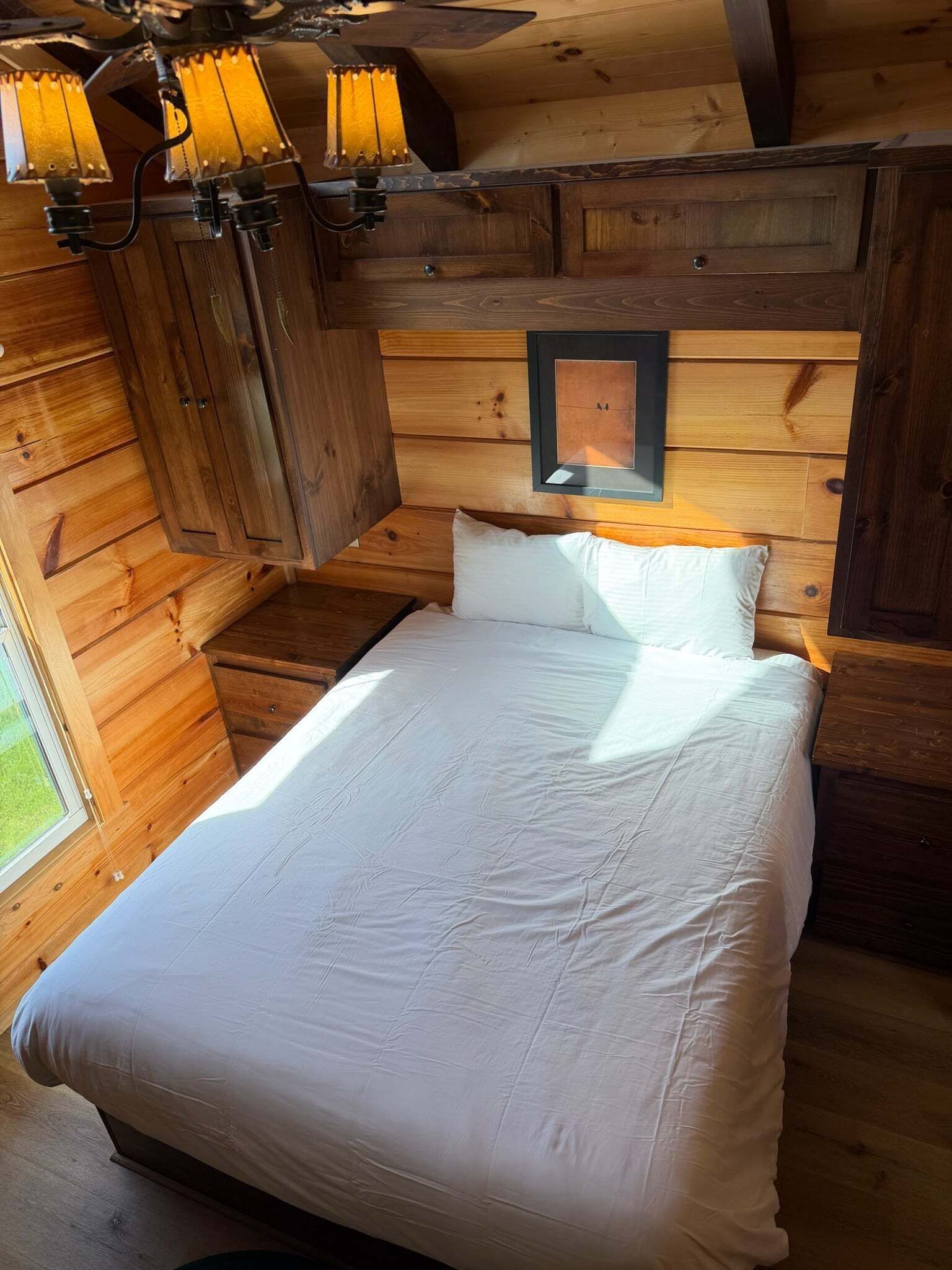 A wooden cabin bedroom with a bed, a nightstand, and a wall-mounted light fixture.