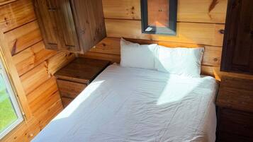 A wooden cabin bedroom with a bed, a nightstand, and a wall-mounted light fixture.