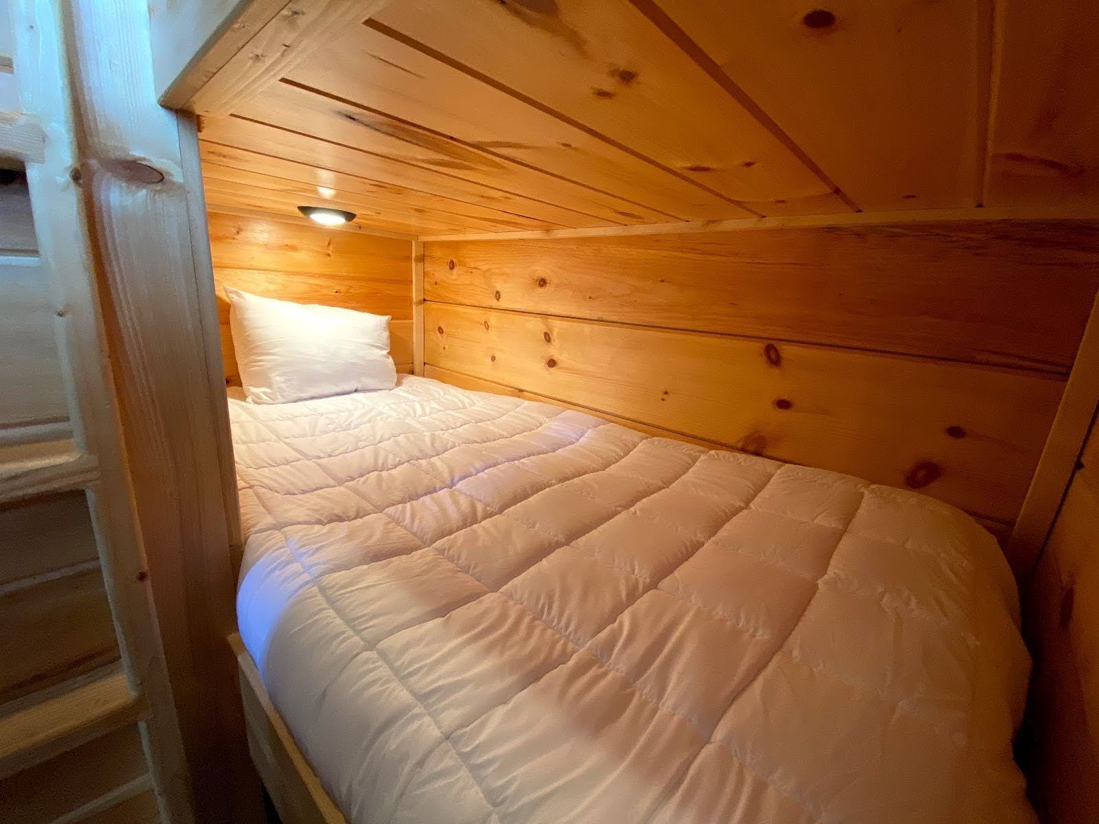 A wooden cabin room with a bed, a wooden ceiling, and a small window.