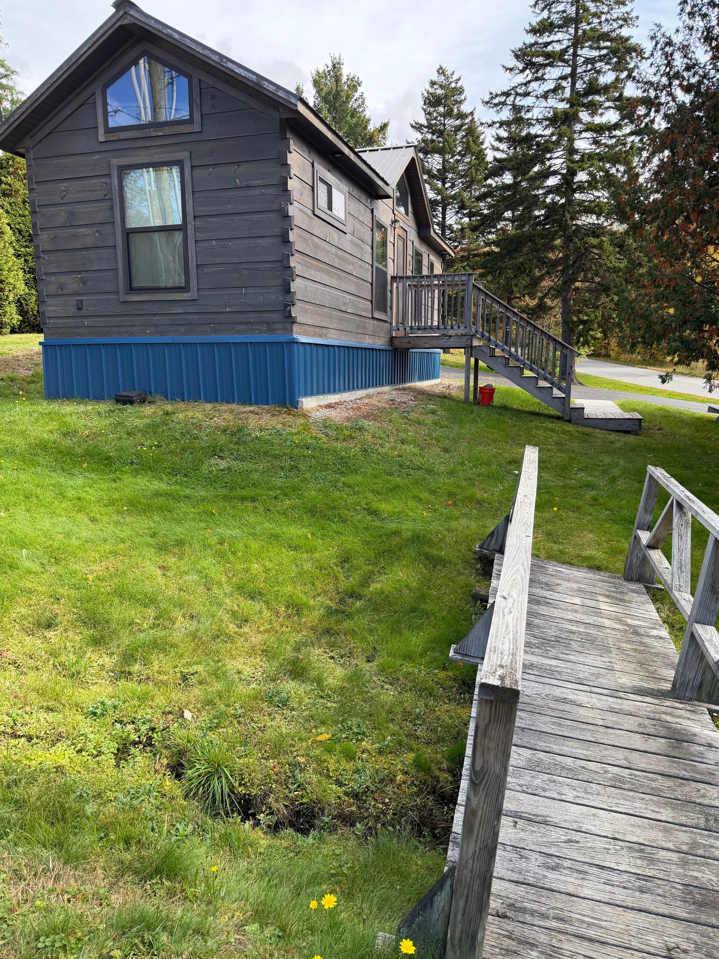 A two-story wooden house with a blue base, a wooden deck, and a staircase leading to a porch.