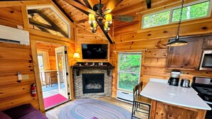 A cozy cabin interior with a fireplace, wooden walls, a television, and a dining area. - B11 Awesome "Tiny Home" A/C, Mountain Views, Minutes to Skiing, Hiking, Attractions, Dog Friendly! (Twin Mountain)