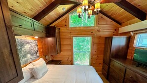 A wooden cabin bedroom with a bed, a window, and a chandelier. - B11 Awesome "Tiny Home" A/C, Mountain Views, Minutes to Skiing, Hiking, Attractions, Dog Friendly! (Twin Mountain)