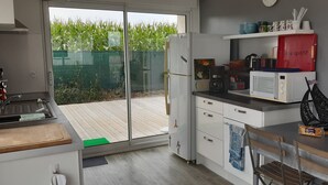 A modern kitchen with a sliding glass door leading to a wooden deck, a refrigerator, a microwave, and various kitchen utensils. - Ocean, beaches, kitesurfing, surfing 400 m away, ground-floor apartment with very large terrace  (Guidel)