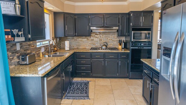 A modern kitchen with dark cabinetry, a granite countertop, stainless steel appliances, and a patterned backsplash.