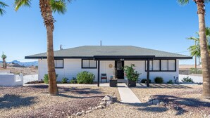 A modern two-story house with a gravel driveway, palm trees, and a clear blue sky.
