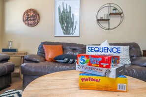 Una sala de estar con un sofá de cuero marrón, una mesa de centro redonda de madera y varios juegos de mesa apilados sobre ella.